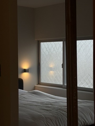 Upper Suite: a bedroom lit by a wall lamp beside a patterned-glass window