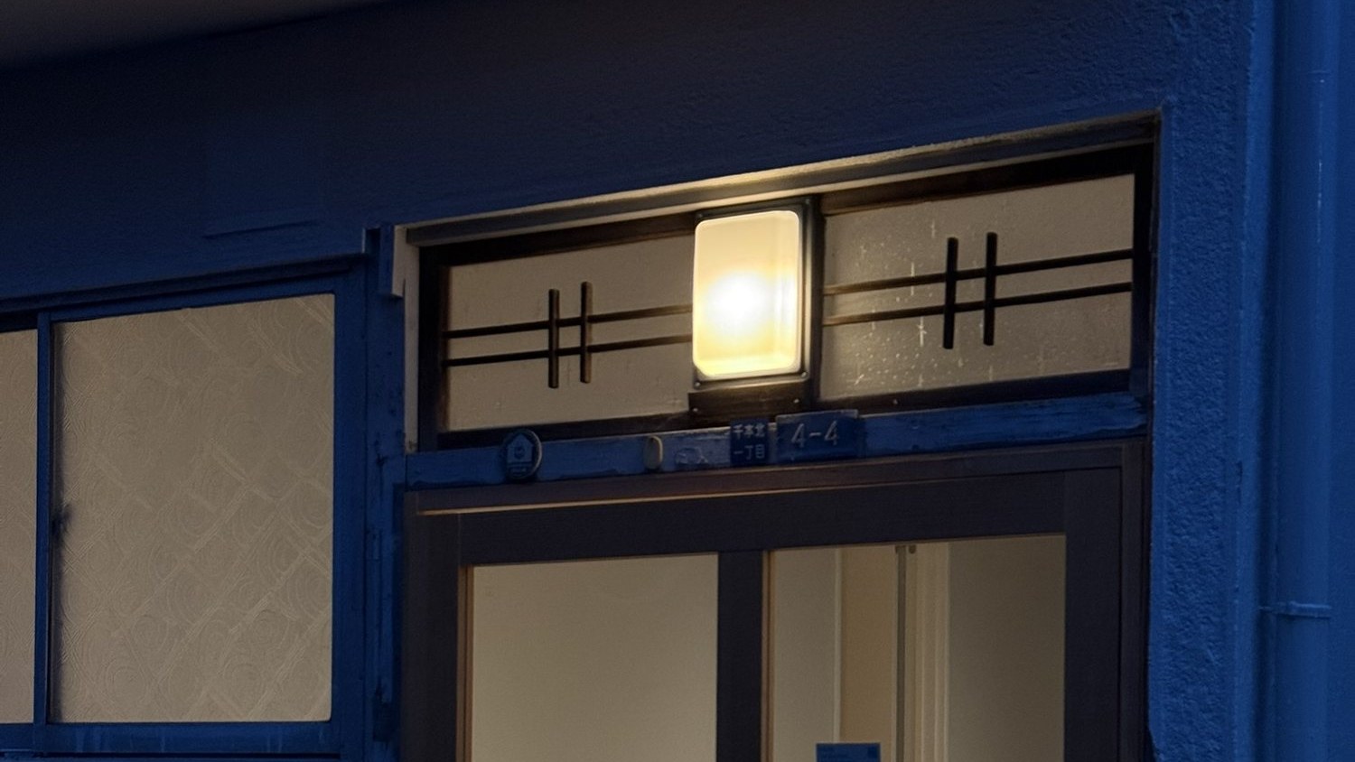 The entrance at dusk: the original transom and its lamp lit above a new timber door frame