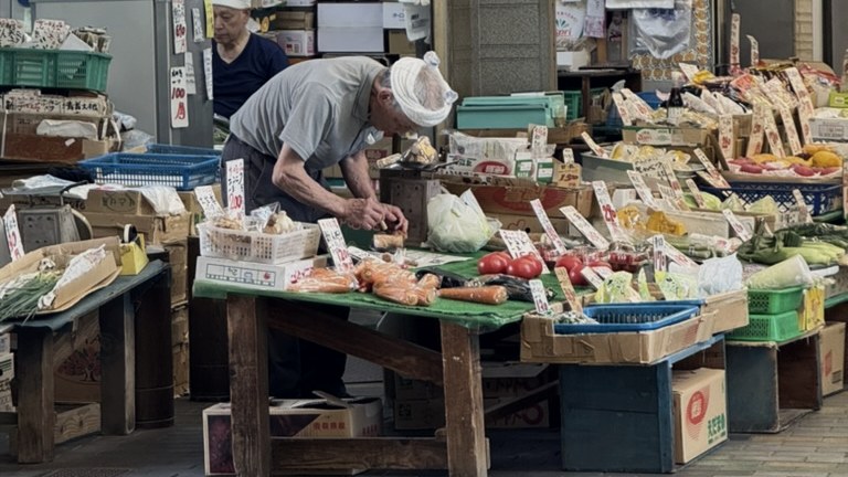 A greengrocer laying out vegetables under a shōtengai awning